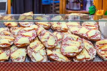 Rustic bread slices topped with melted cheese and bacon displayed at festive food stall. Concept of comfort food, hearty snack, winter street flavors
