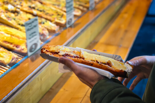 Hand holding hot baguette with cheese. Person holding cheesy baked baguette with melted toppings in takeaway tray, holiday food market stall. Concept of baguette, street fast food, Christmas market