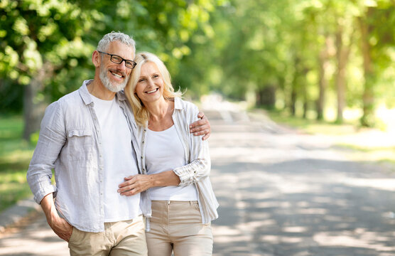 Beautiful mature spouses hugging outdoors while walking in summer park, happy senior couple embracing and looking away, older husband and wife enjoying time together, having romantic date outside