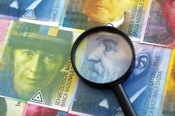 Swiss franc banknotes and magnifying glass. The francs money bills with loupe lies on table