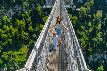 Mother and daughter child girl on a suspension bridge in a skypark in Sochi, summer travel and entertainment with family. © KseniaJoyg