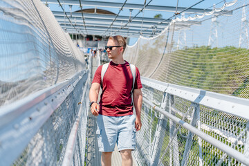 A young man walks on a suspension bridge in a skypark in Sochi, summer travel and entertainment.