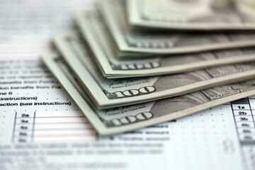 Big amount of United States hundred dollar bills on table with tax return form close up