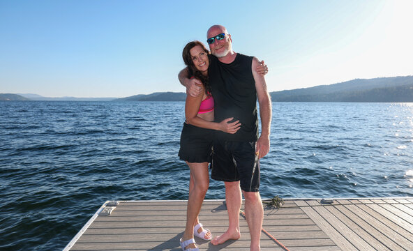 Happy married couple together on a boat dock at coeur D'Alene lake in Harrison, Idaho, USA. The man is bald with a beard and the woman is wearing a bikini top and swim skirt. The two people are happy.