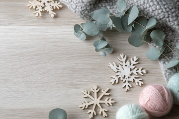 A cozy winter flat lay featuring wooden snowflakes, eucalyptus, and pastel yarn on a light wooden background.