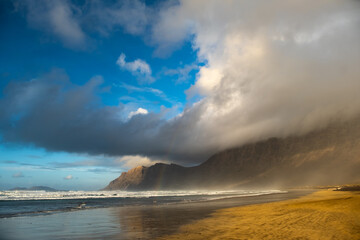 Majestic clouds roll over Famara Beach on Lanzarote, creating a dramatic scene against the striking...