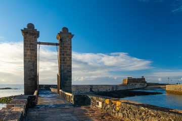 Stone bridge leading to the Castillo de San Gabriel in Arrecife, Lanzarote, and calm ocean. The...