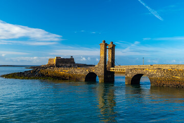 Stone bridge leading to the Castillo de San Gabriel in Arrecife, Lanzarote, and calm ocean. The...