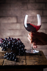 Red wine glass in a men hand and ripe grapes on wooden background