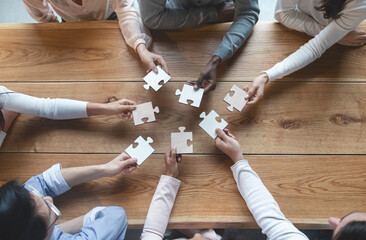Fototapeta na wymiar Startup and teamwork concept, top view of creative multiracial team sitting at table and putting together puzzle pieces