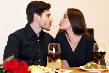 Romantic Date Concept. Smiling handsome couple making spaghetti kiss, sharing plate of tasty...