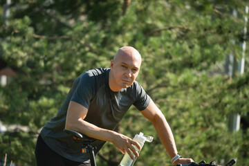 Caucasian adult cyclist tired, and relax near bicycle at greenery public park. Relaxation and...
