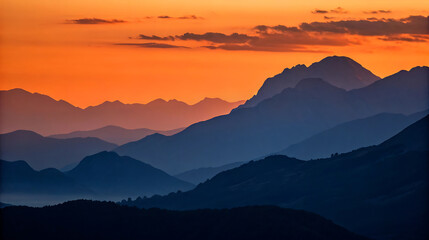Fototapeta premium Silhouetted mountains fade into the distance at sunset with orange sky