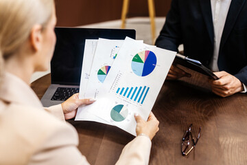 Businesswoman presenting financial reports with colorful graphs and charts to a colleague during a strategic planning meeting in a modern office environment