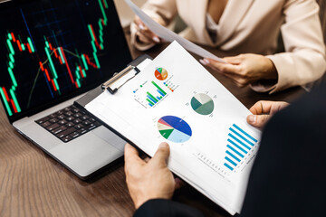 Business professionals analyzing financial charts and graphs on a clipboard and laptop during a strategic planning meeting in a modern office environment