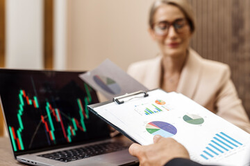 Business professionals engaged in a meeting, analyzing financial data on a laptop and presentation...
