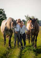 Best friends spending time together in green field with their horses, laughing, enjoying each...