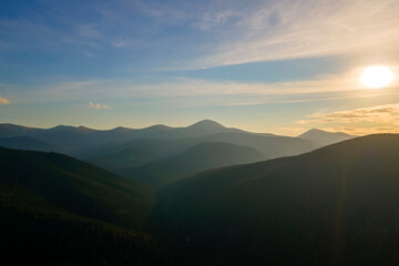 Fototapeta premium Aerial view of dark mountain hills with bright sunrays of setting sun at sunset. Hazy peaks and misty valleys in evening
