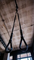 panoramic low angle view of hanging trx bands against concrete ceiling with moody gym lighting