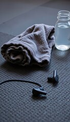 detail shot of textured gym flooring with dropped towel, water bottle, and bluetooth earbuds
