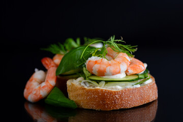 Small canapes with shrimps, salad and cucumbers on a black background