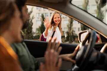 Happy mother and father bringing their daughter to school, sitting in car and smiling, saying...