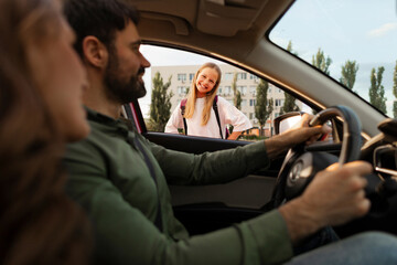 Parents dropping off their daughter in front of school, happy schoolgirl looking at parents and...