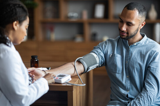 Middle eastern young man having regular checkup at general practitioner at modern clinic, african american woman doctor checking heart rate for male patient suffering from hypertension, copy space