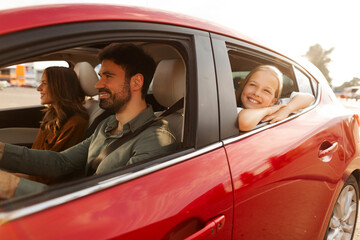 Happy girl looking out of car window and smiling, riding with parents in automobile across city. Auto traveling and road adventure concept