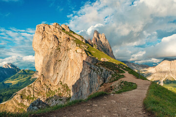 Dramatic cliffs and hiking trail on Seceda mountain in Italian Dolomites Alps at sunset, Trentino Alto Adige, Italy. Mountain landscape with jagged peaks under cloudy sky in Dolomiti, South Tyrol.
