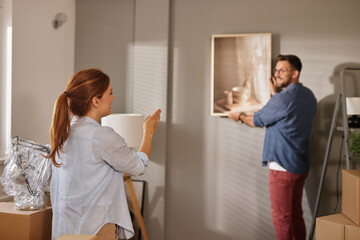New homeowners are organizing their living space by unpacking boxes and hanging artwork. Afternoon...