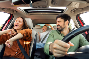 Joyful European family young parents and daughter enjoying car journey, listening music, singing...