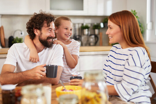 Parents and child are gathered around a kitchen table, engaging in cheerful conversation while sharing breakfast. The atmosphere is warm and joyful.