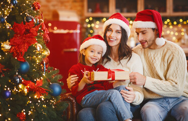 Happy little girl holding desirable Christmas gift, celebrating xmas with parents at home