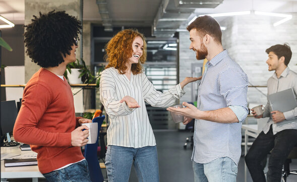 Very friendly girl hugging young man, welcoming new member of creative team in modern office