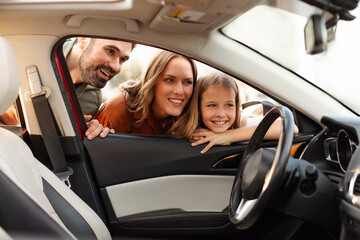 Happy family of three buying new car, looking through window at auto interior, choosing automobile in dealership, show view from inside vehicle