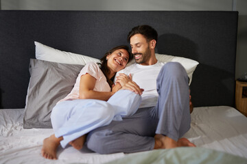 A man and woman are sitting closely together on a bed, laughing and enjoying each other's company...