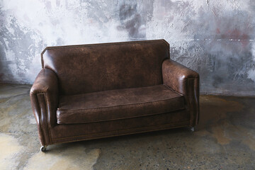 Vintage brown leather sofa against textured wall for rustic interior design and furniture catalog