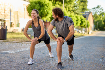 Two individuals participate in a partner stretching exercise in an urban park setting. The sun...