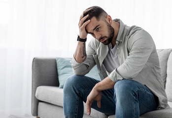Man sit alone feeling sad worry regret or fear, depressed and desperate in sofa at home. Suffering...