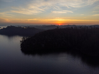 Fototapeta premium Orange sun setting between mountains behind large lake