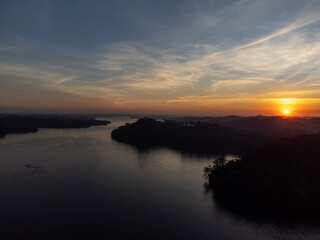 Fototapeta premium Orange sun setting between mountains behind large lake