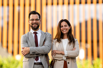 Portrait of smiling business people with arms crossed in front of modern office building