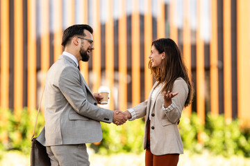 Business people shaking hands outdoors holding coffee and smiling