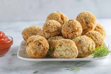 Crispy potato croquettes with tuna, cheese and dill on white plate beside ketchup.