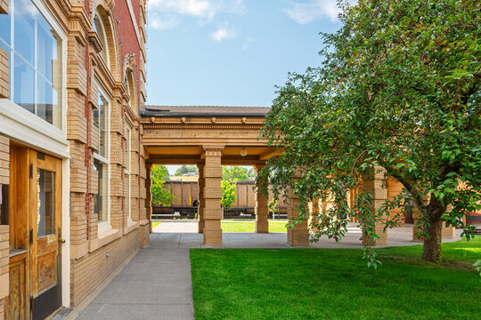 A train is visible behind the covered colonnade walkway of the 1902 Livingston Depot Center train station, in the historic downtown district of Livingston, Montana.