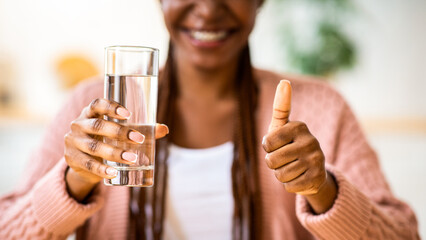 Healthy Refreshment. African American Woman Holding Glass With Mineral Water In Kitchen And Showing Thumb Up, Unrecognizable Black Lady Taking Care About Body Hydration, Cropped Image, Closeup