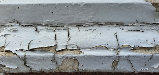 Close-up of cracked and peeling white paint on an old concrete surface. The texture reveals layers...