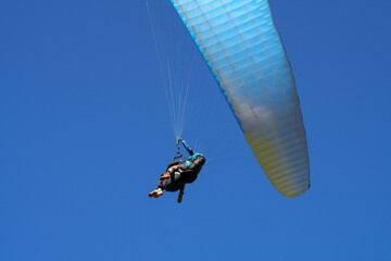 Flight of a passenger with an instructor on a paraglider. Fragment of a wing on a blue background.