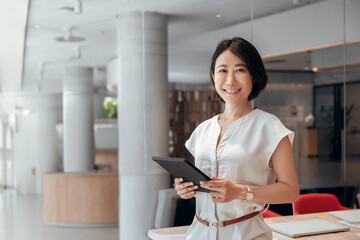 Middle-aged eastern businesswoman holding digital tablet using tab application in office, looking...